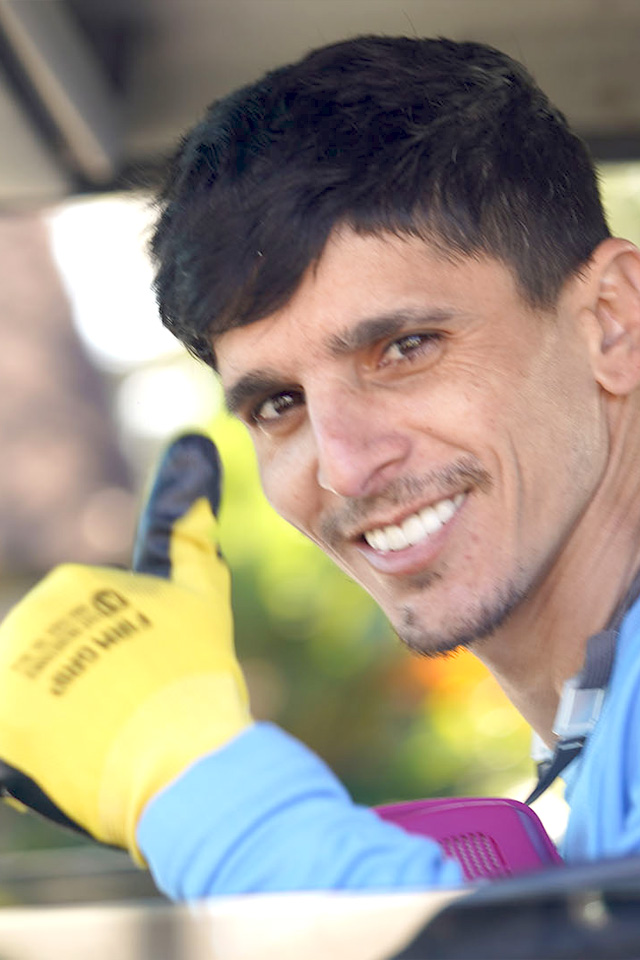 Discrete pest control service Smiling man with short dark hair in a blue shirt giving a thumbs-up while wearing yellow work gloves.